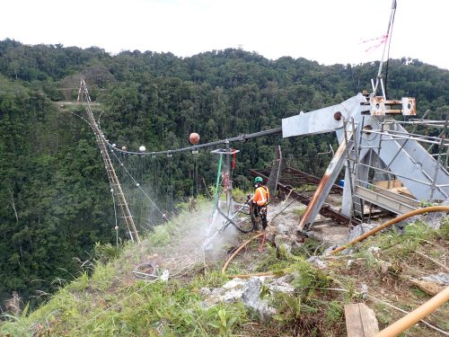 Rope access worker at a construction site with industrial equipment in the process of bridge maintenance, overlooking a lush forest valley.